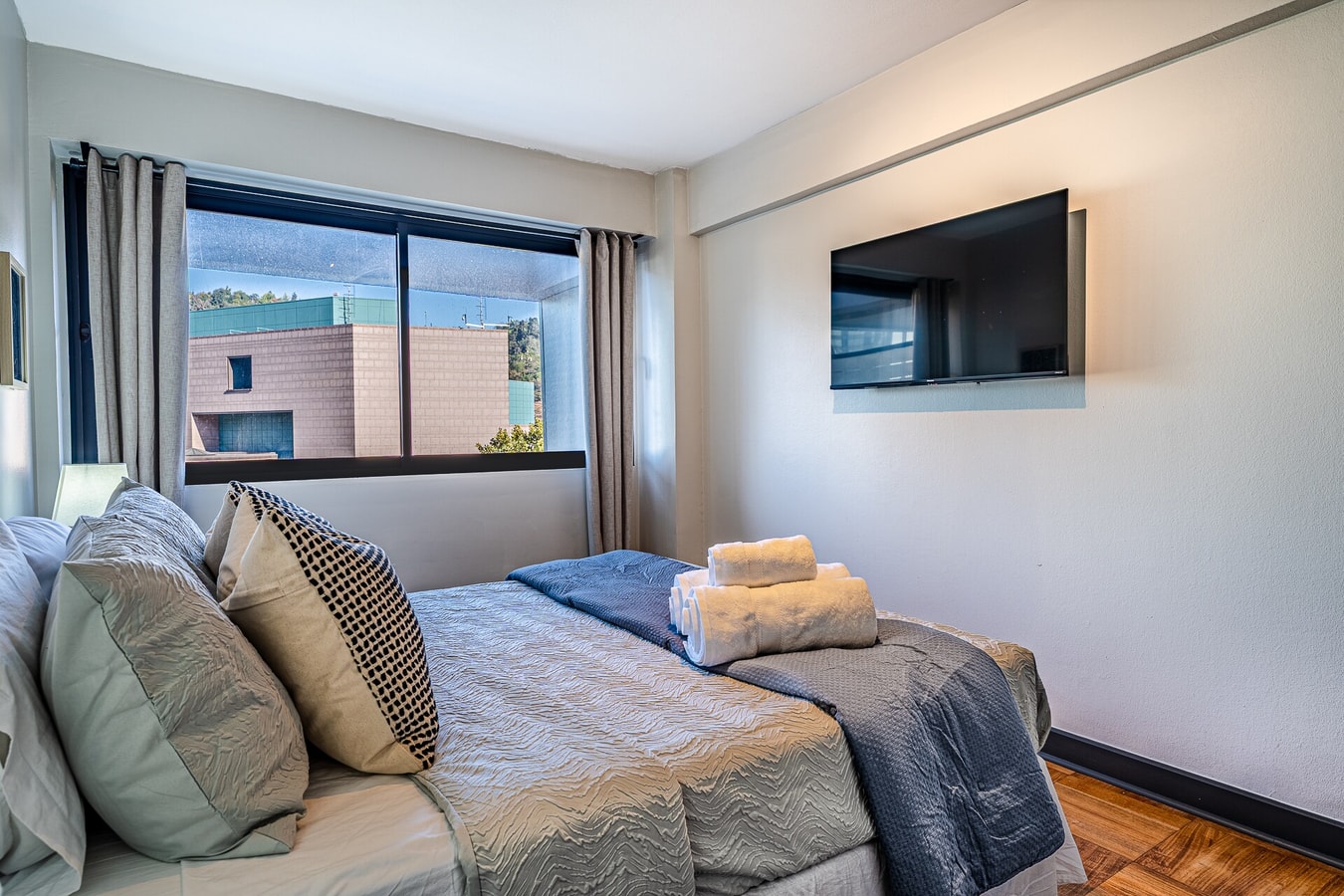 Dormitorio con cama matrimonial, escritorio, silla y ventana con cortina lateral