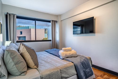 Dormitorio con cama matrimonial, escritorio, silla y ventana con cortina lateral