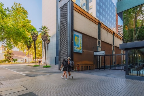 Fachada de acceso del edificio, con reja y personas caminando por la vereda