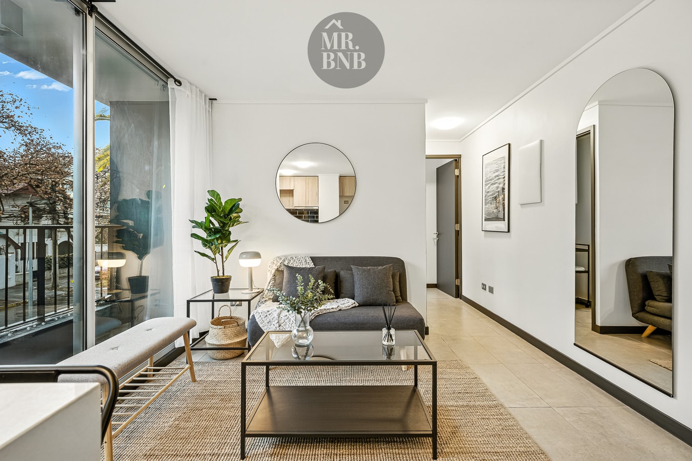 Living con sofá, banca, espejos redondos en la pared y alfombra sobre piso de madera