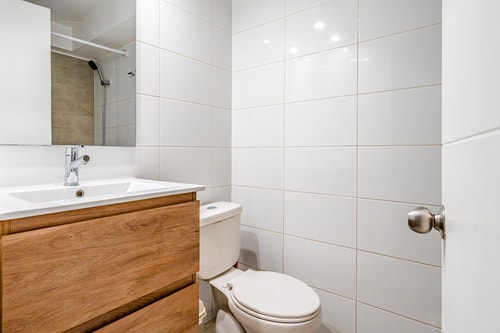 Baño con lavamanos sobre mueble de madera, espejo e inodoro.