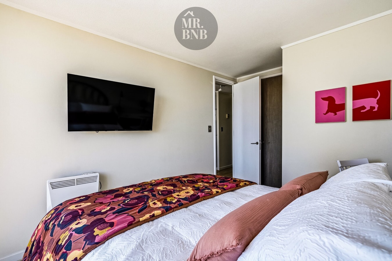 Dormitorio con cama, cubrecama floral, TV montada en la pared y cuadros decorativos