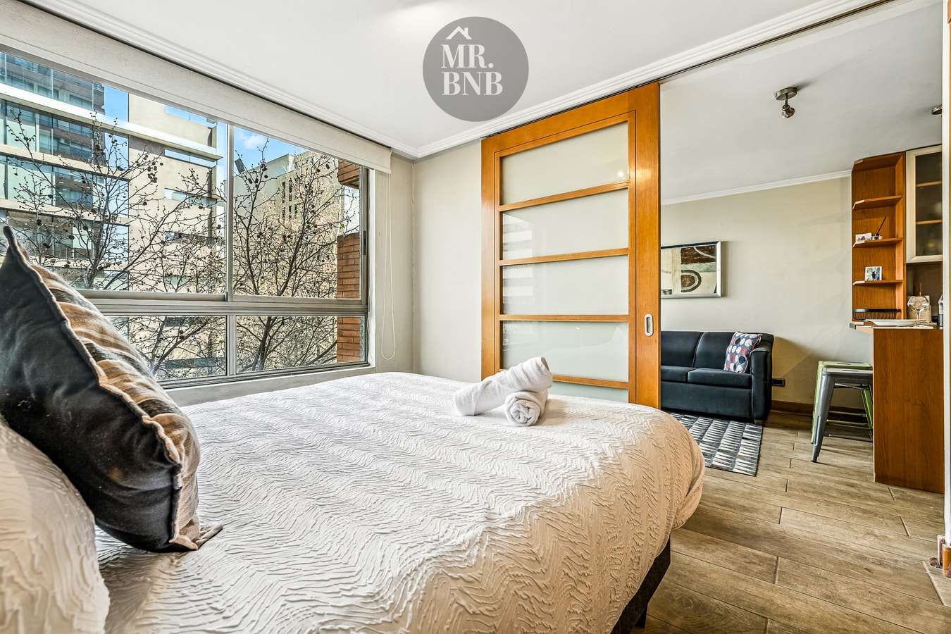 Dormitorio con cama y puerta corrediza hacia el living con sofá y repisas