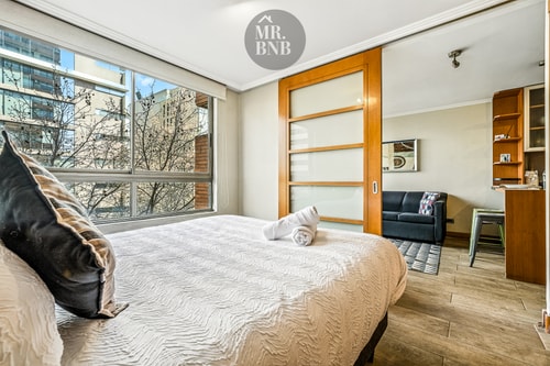 Dormitorio con cama y puerta corrediza hacia el living con sofá y repisas