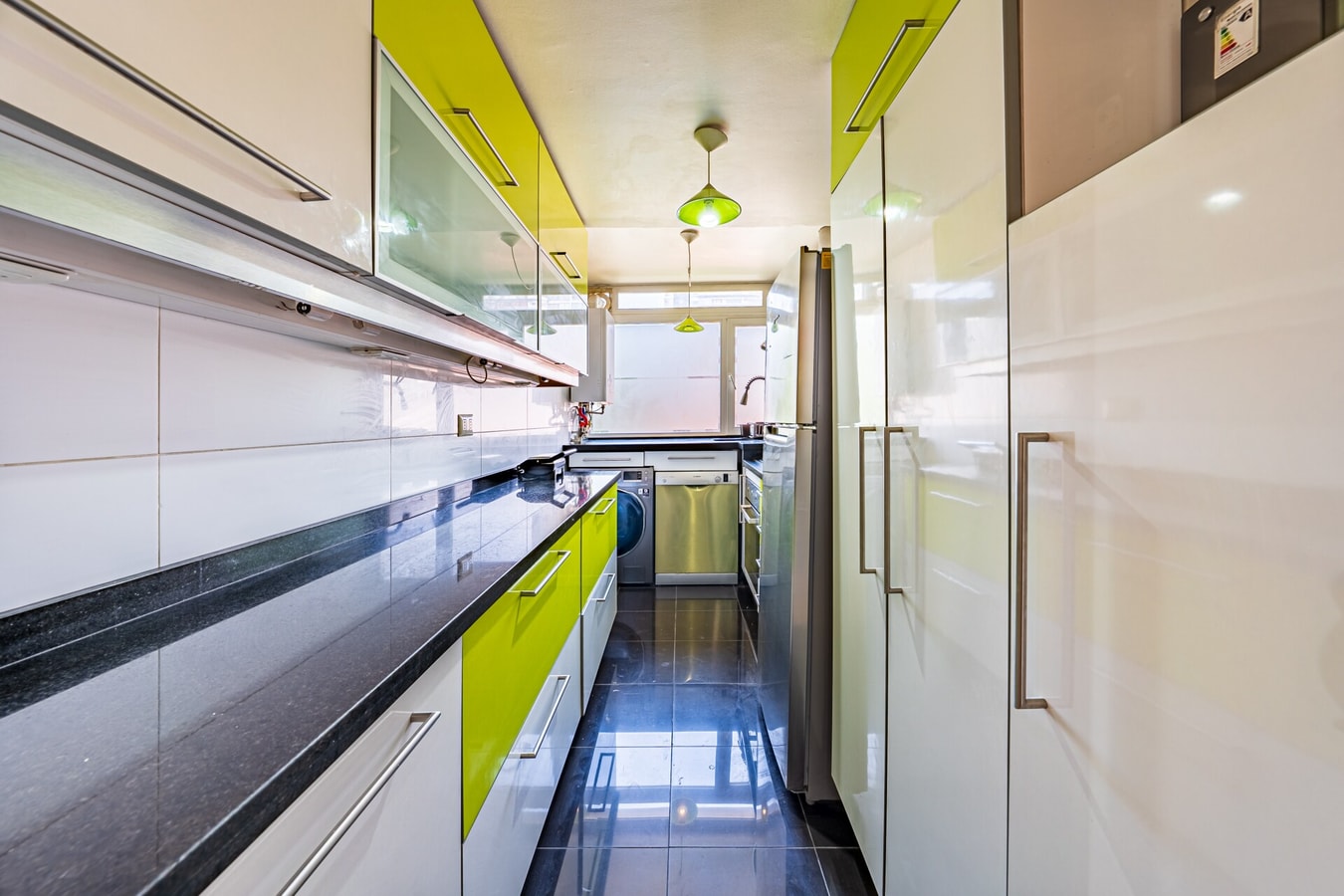 Cocina en formato pasillo con muebles brillantes verde lima y blanco, y mesón de granito negro.