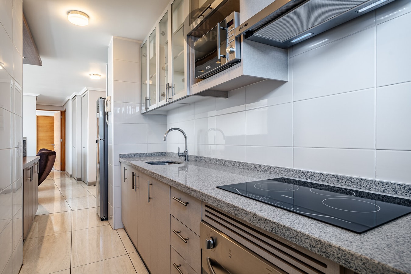 Cocina en ángulo de pasillo, encimera de granito, cooktop y campana