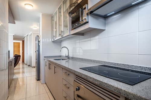 Cocina en ángulo de pasillo, encimera de granito, cooktop y campana