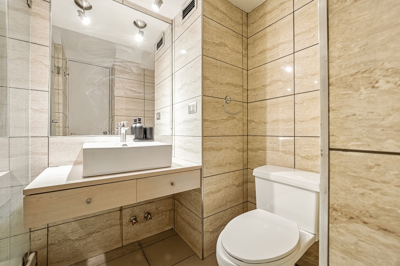 Baño con mueble vanitorio, espejo grande, ducha e inodoro en tonos beige