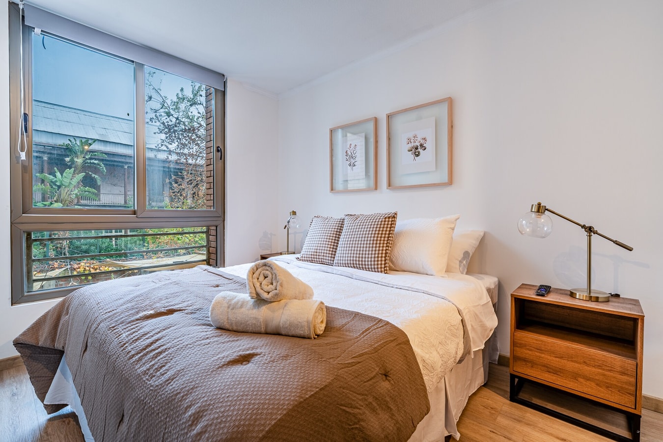 Dormitorio con cama, velador de madera y ventana hacia el exterior