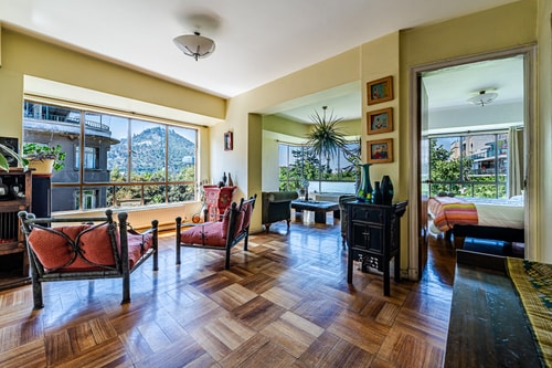 Living con sillones de mimbre y cojines, mesas y ventanales, piso de parquet