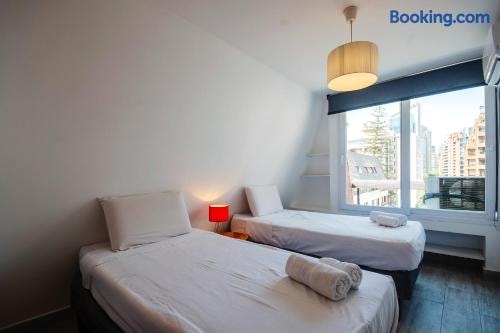 Dormitorio con cama, veladores con lámparas encendidas, ventana con vista a la ciudad
