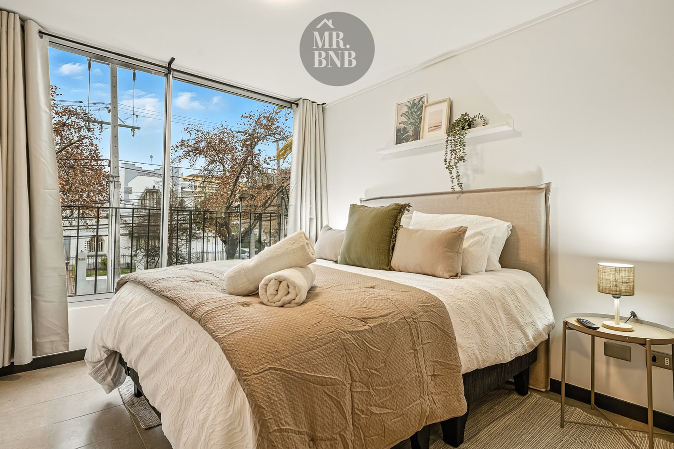 Dormitorio con cama de dos plazas, ropa de cama en tonos beige y ventana con vista a árboles