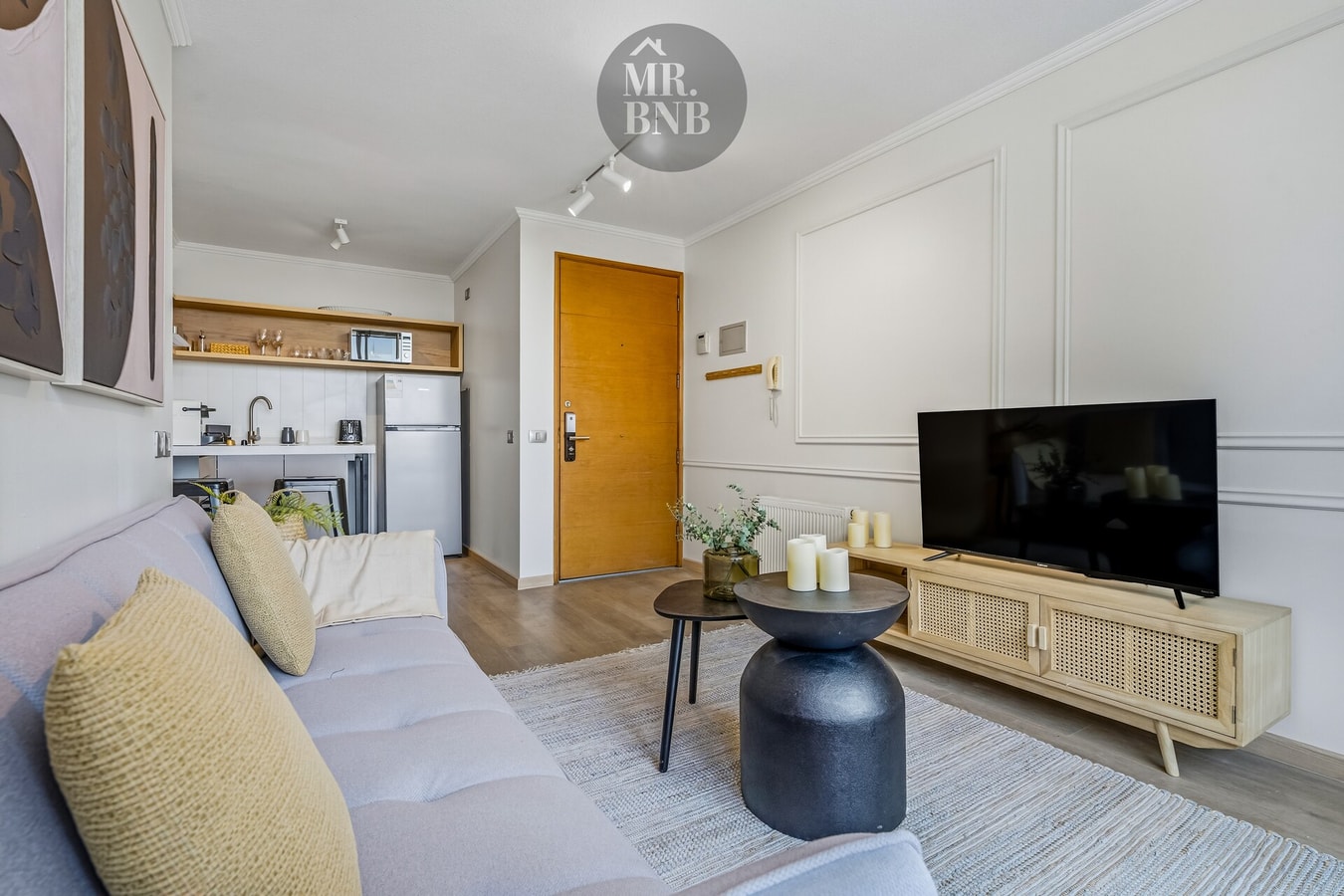 Living con sofá claro, mesas auxiliares y cocina al fondo con puerta naranja