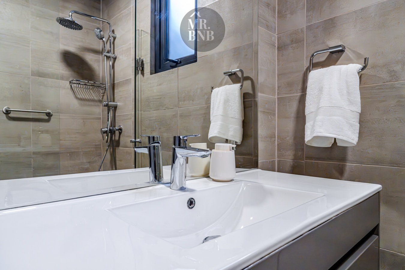 Detalle de baño con lavamanos y ducha, toallas colgadas