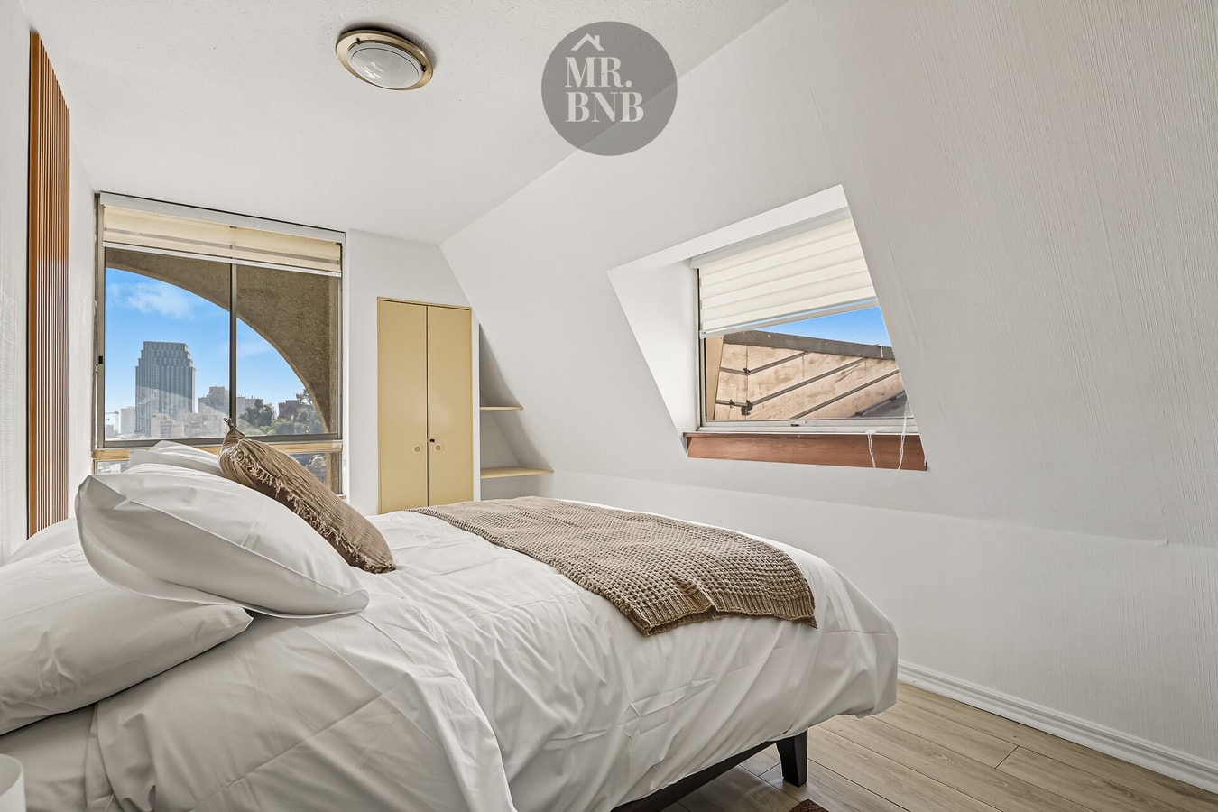 Dormitorio bajo techo mansarda con cama y ventana con vista a la ciudad