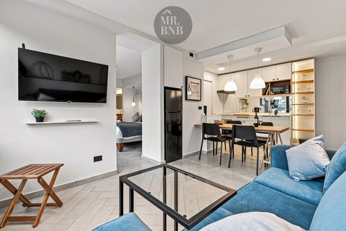 Living con sofá azul, mesa de centro y comedor con cocina al fondo.