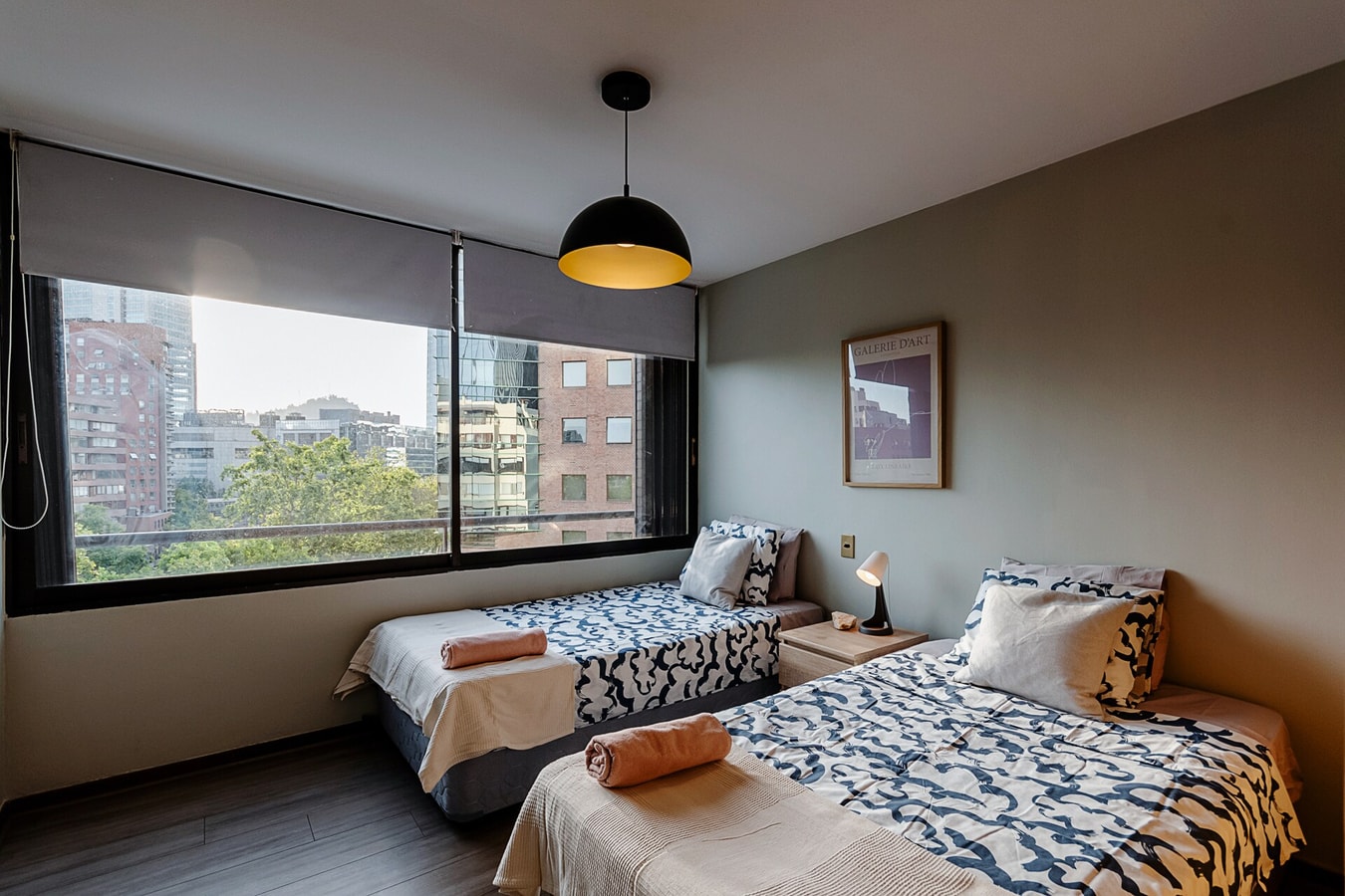 Dormitorio con dos camas individuales, ventana con vista y cuadro decorativo.
