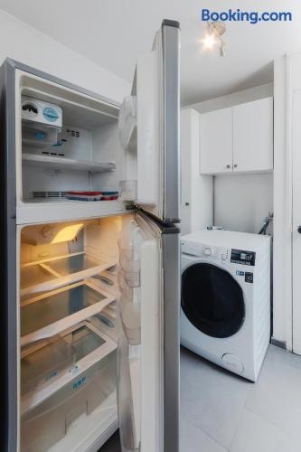 Refrigerador de dos puertas abierto y, al fondo, la lavadora del departamento en el área de servicio con muebles blancos