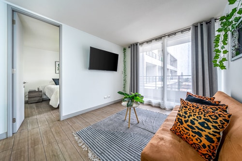 Living con sofá, televisor de pantalla plana, ventanal con cortinas grises y planta decorativa