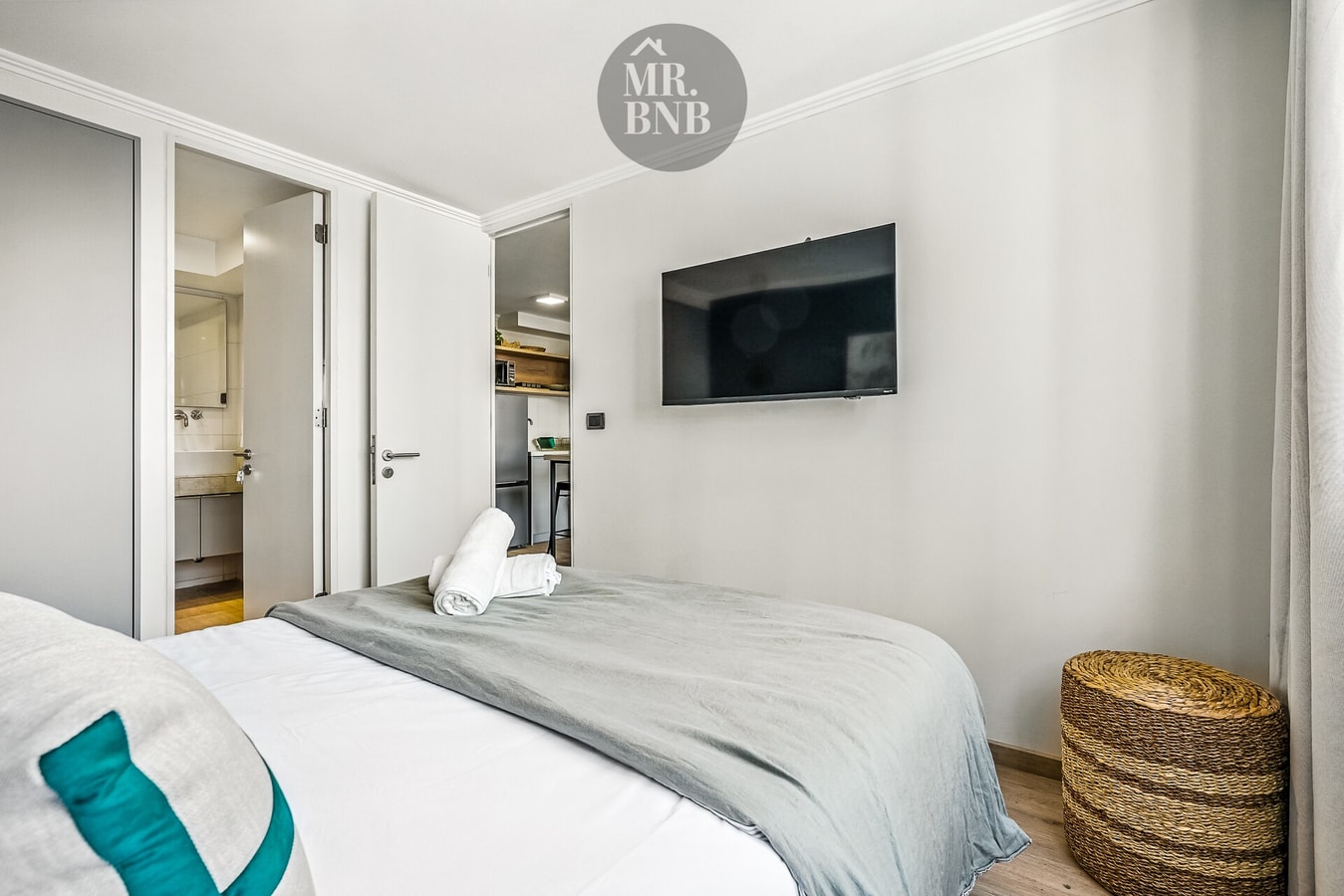 Dormitorio con cama, televisor en la pared y puerta hacia el baño.