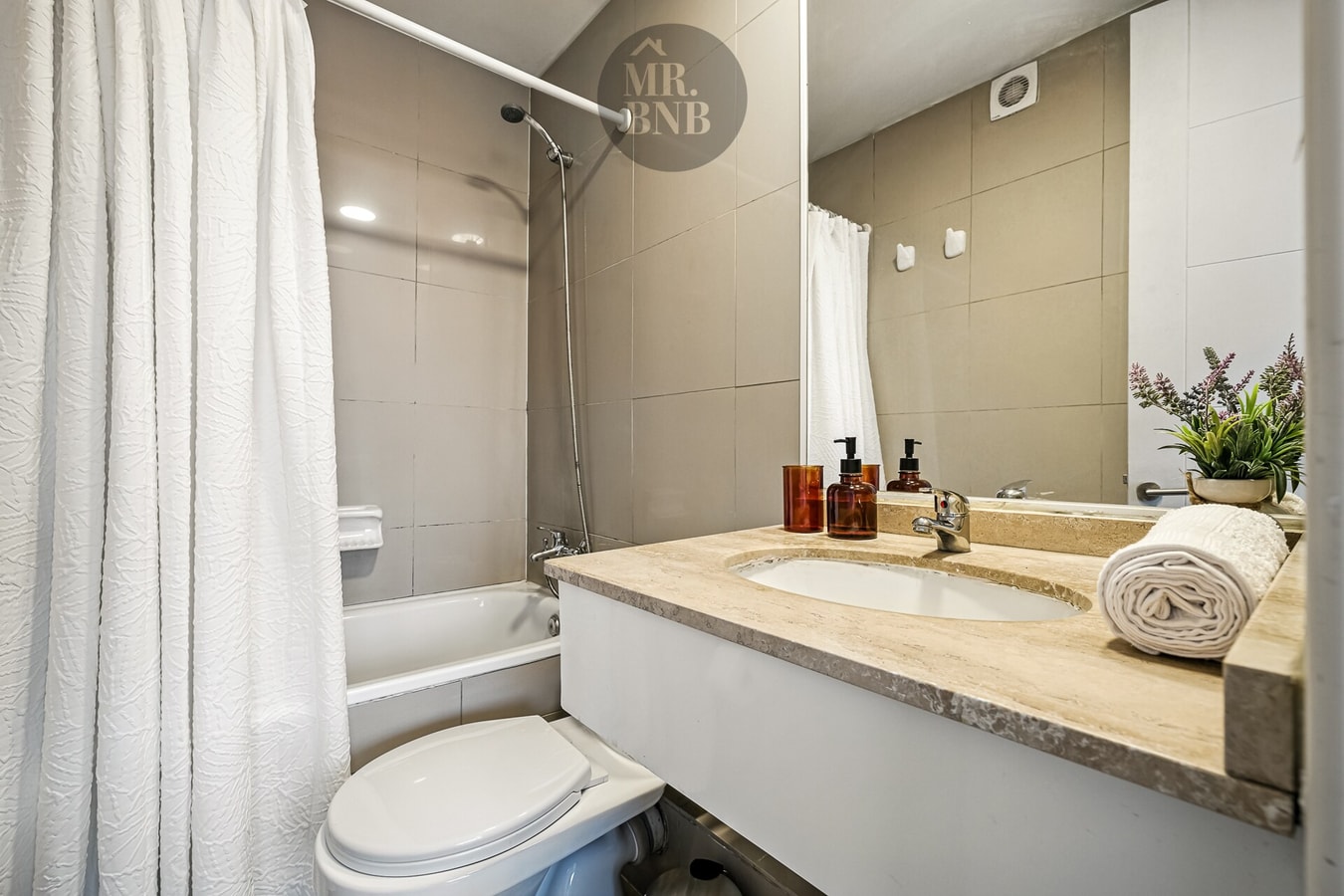 Baño con tina, cortina, mueble vanitorio y artículos de aseo dispuestos