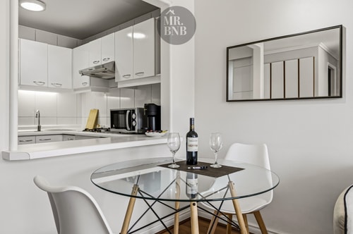 Cocina blanca con campana extractora y mesa de comedor con sillas junto a la ventana.