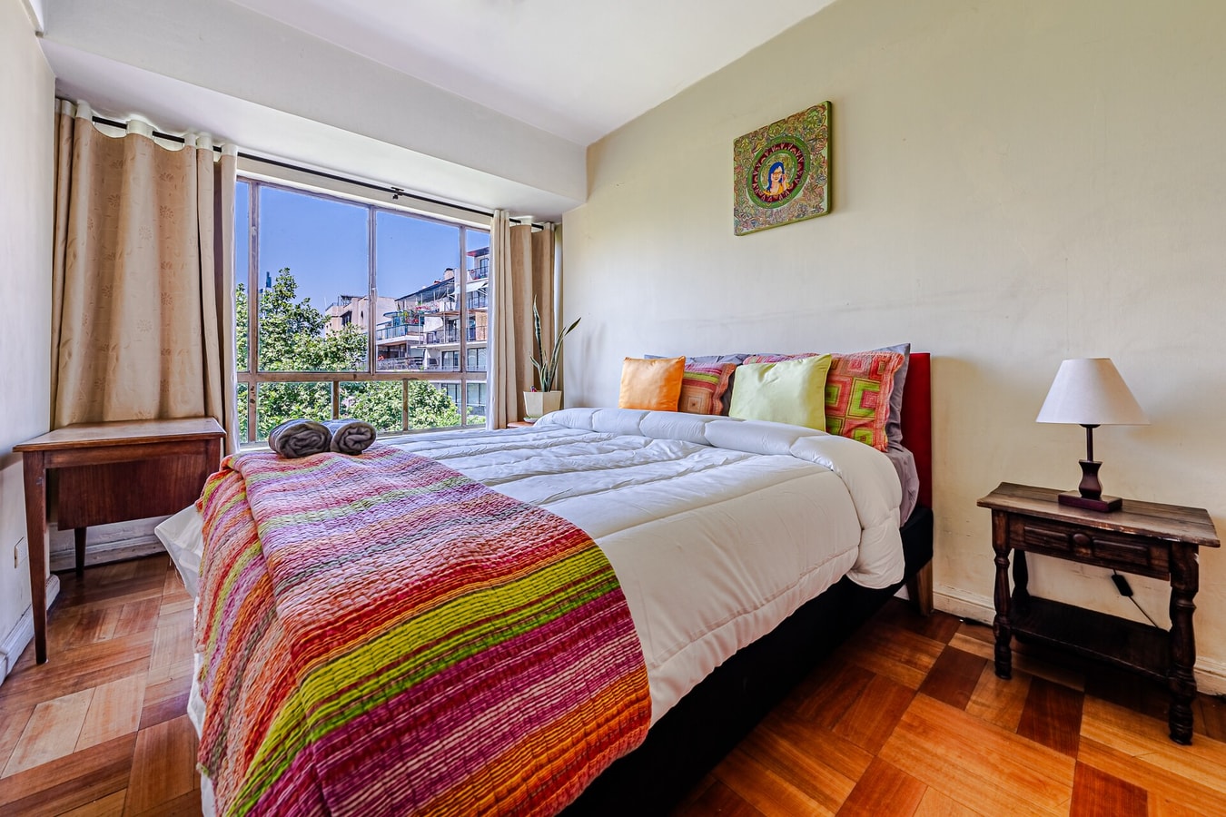 Dormitorio con cama matrimonial, cubrecama a rayas de colores, cómoda antigua y cuadro