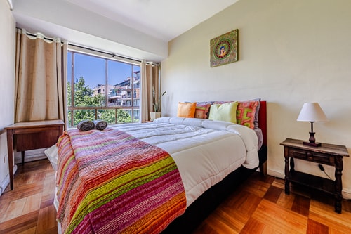 Dormitorio con cama matrimonial, cubrecama a rayas de colores, cómoda antigua y cuadro