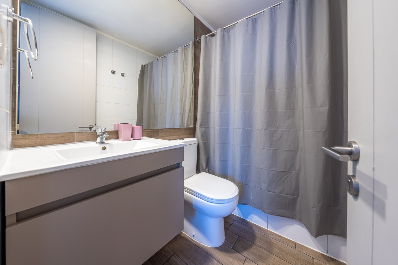Baño con tina, cortina gris, lavamanos con espejo e inodoro