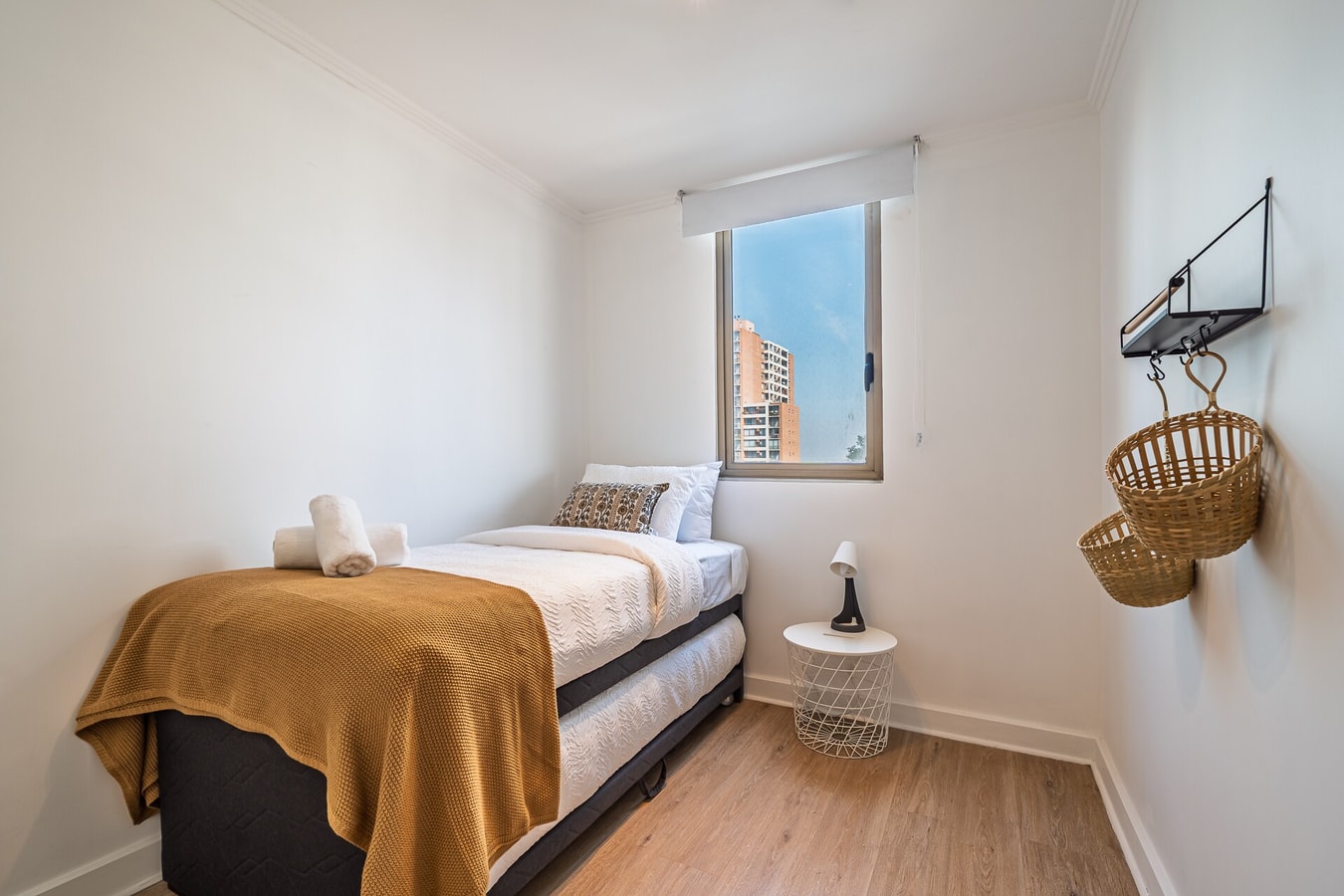 Dormitorio pequeño con cama individual y repisa con cesto de mimbre