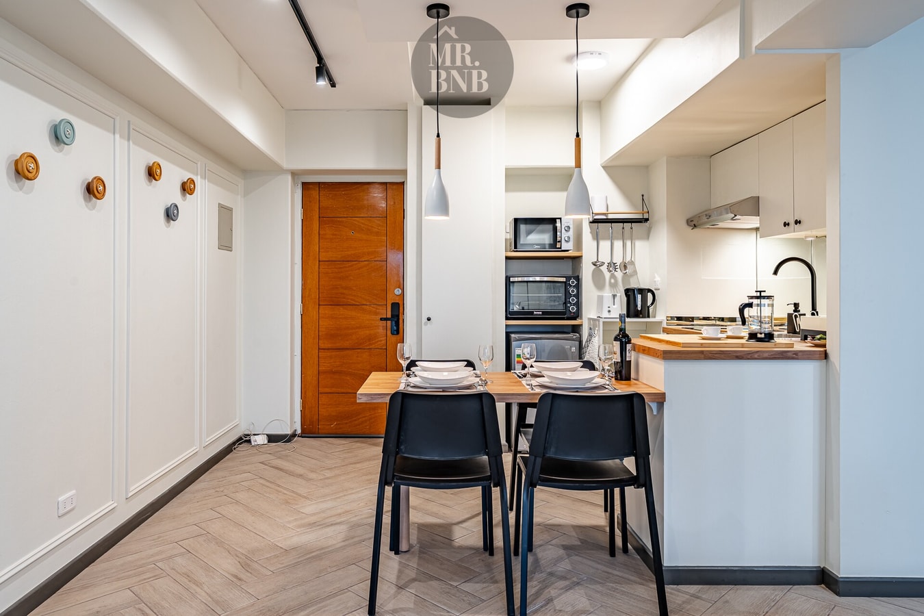 Comedor con mesa y sillas negras, cocina al fondo y puerta de entrada