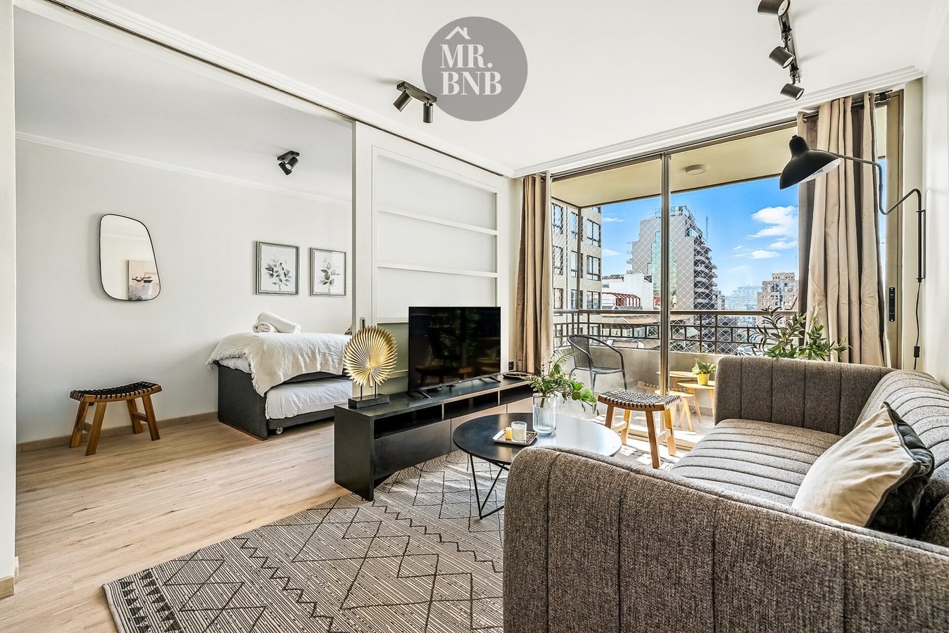 Living con sofá gris, mesa de centro, televisor y ventanal con vista a la ciudad.