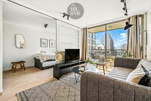 Living con sofá gris, mesa de centro, televisor y ventanal con vista a la ciudad.