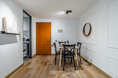 Comedor con mesa, sillas y puerta de acceso junto a espejo redondo