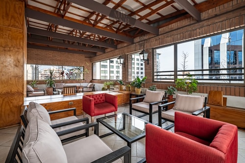 Sala común del edificio en azotea, con techo de madera, sillones rojos y mesa de centro