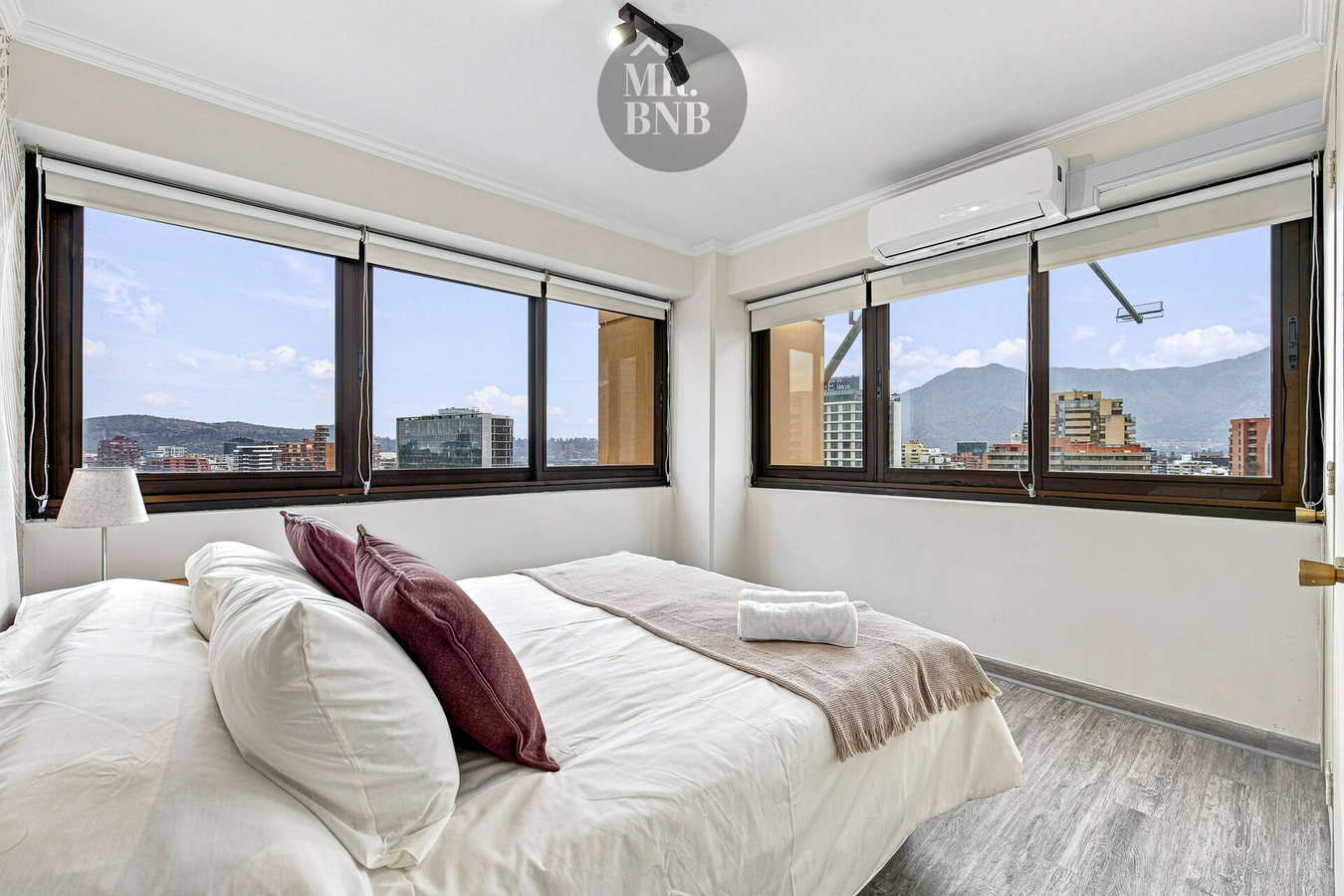Dormitorio con cama de dos plazas, cojines granate, aire acondicionado y ventanales panorámicos.