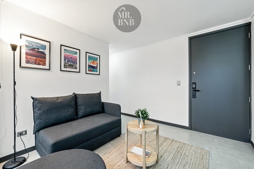 Living con sofá, mesa auxiliar y cuadros en la pared, puerta de acceso al fondo.