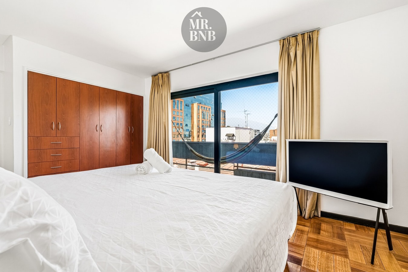 Dormitorio con cama, closet de madera, ventana con vista y hamaca en balcón vecino
