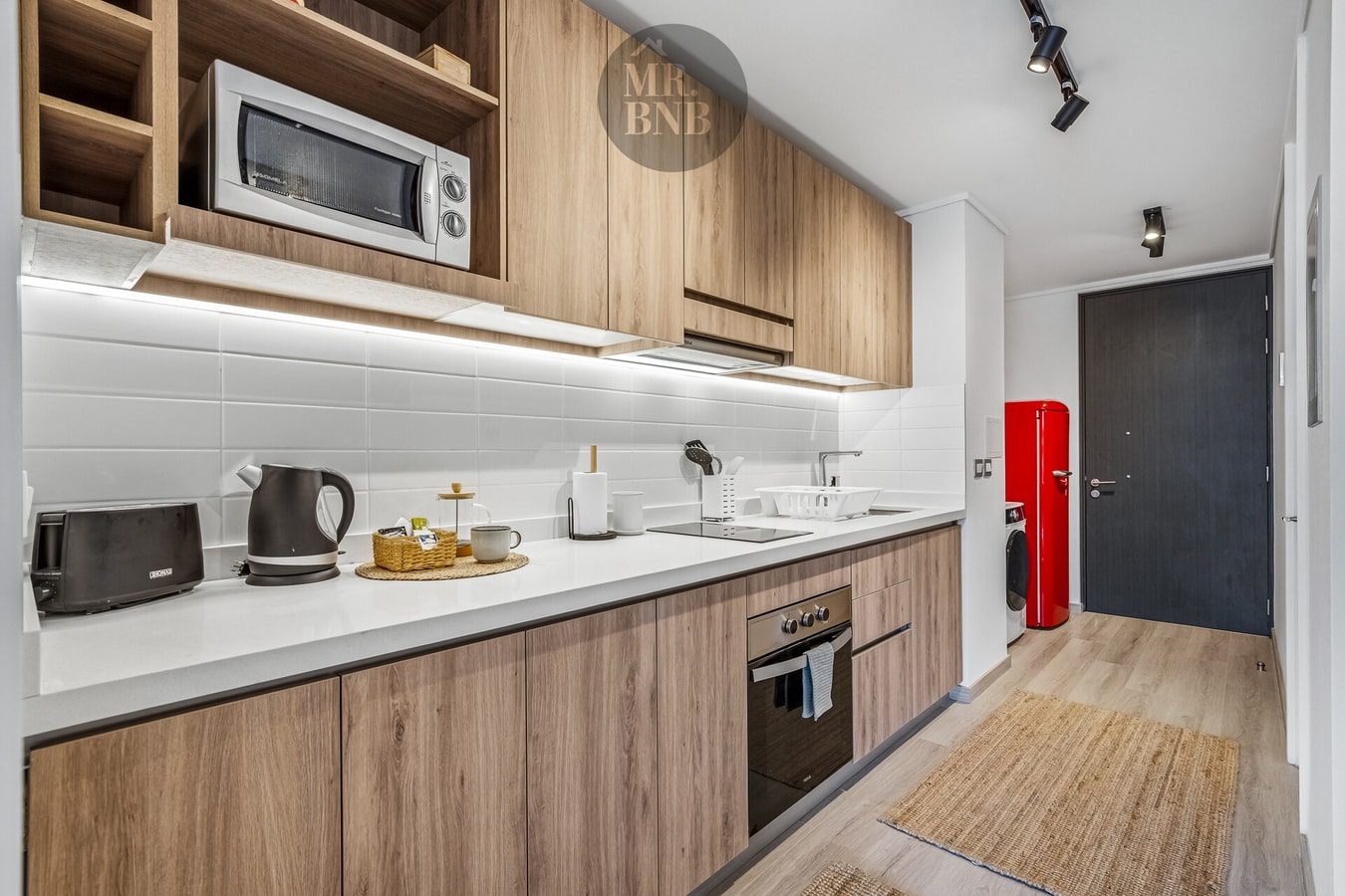 Cocina con muebles de madera, microondas, hervidor y puerta de acceso al fondo