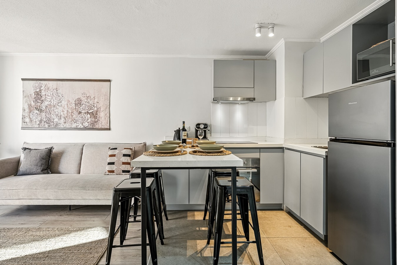 Cocina en línea con muebles claros, comedor con banquetas y refrigerador