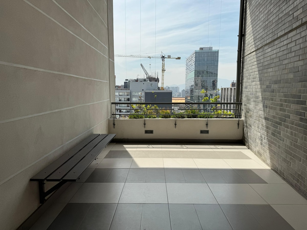 Terraza exterior con banca metálica larga, jardineras y vista a los edificios del centro