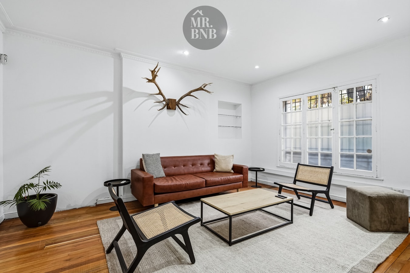 Living con sofá de cuero, mesa de centro y cornamenta decorativa en la pared.