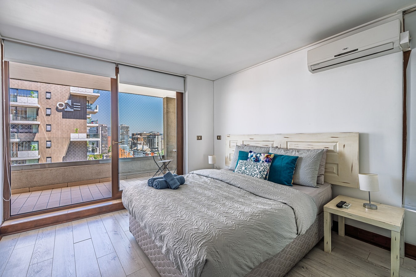 Dormitorio con cama, ventanal hacia edificios y aire acondicionado