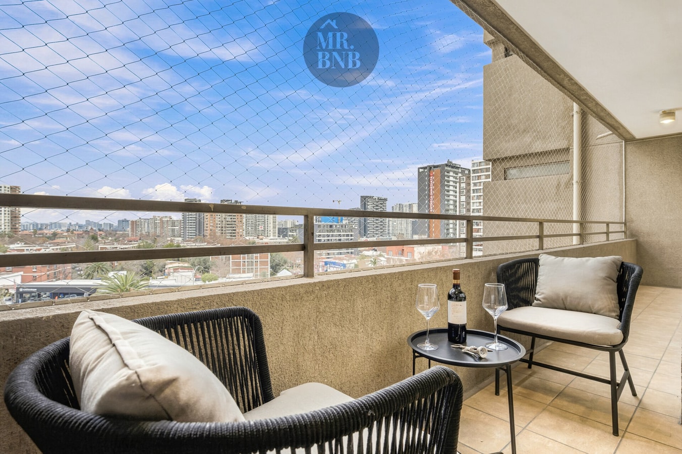 Terraza con sillones de mimbre, mesa auxiliar, vista a edificios y cielo despejado