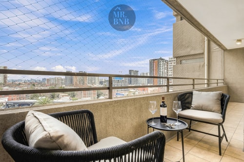 Terraza con sillones de mimbre, mesa auxiliar, vista a edificios y cielo despejado