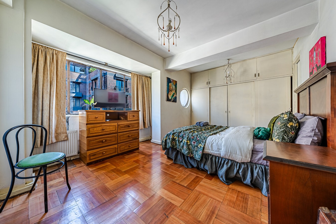 Dormitorio con cama, cómoda, silla y ventana con vista a edificios