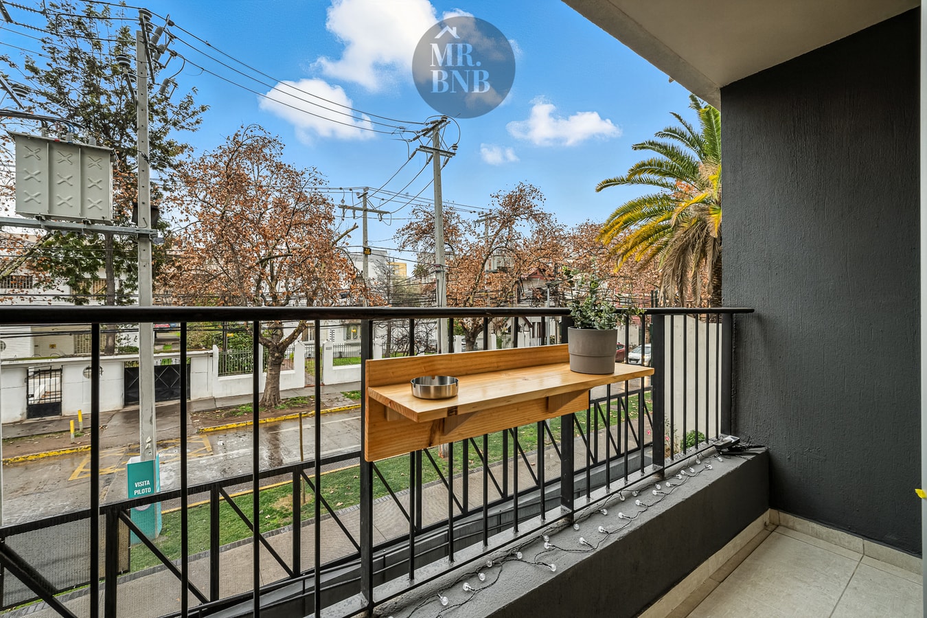 Balcón con mesa de madera abatible y dos sillas, reja perimetral y vista a la calle