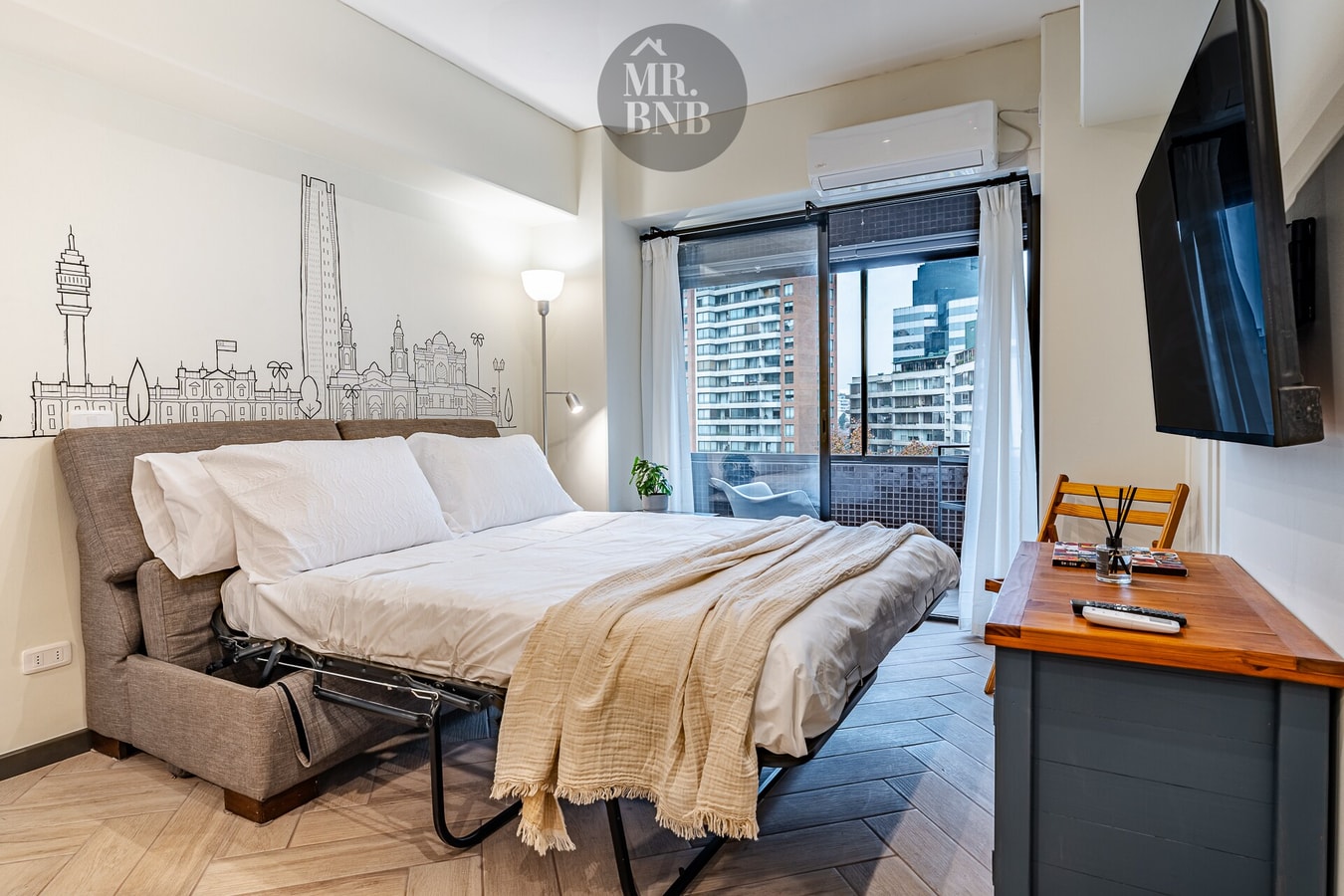Dormitorio con sofá cama desplegado, mural de la ciudad, ventanal con cortina y TV