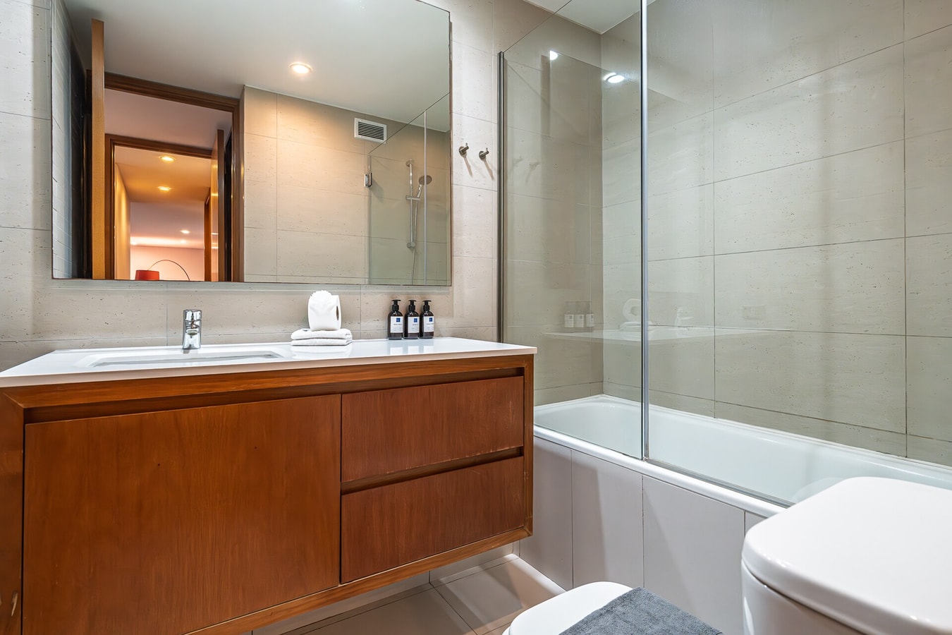 Baño con tina, ducha de vidrio y mueble de vanitorio en madera.