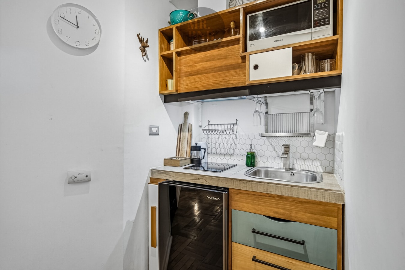 Kitchenette de suite con reloj de pared, microondas y repisas de madera